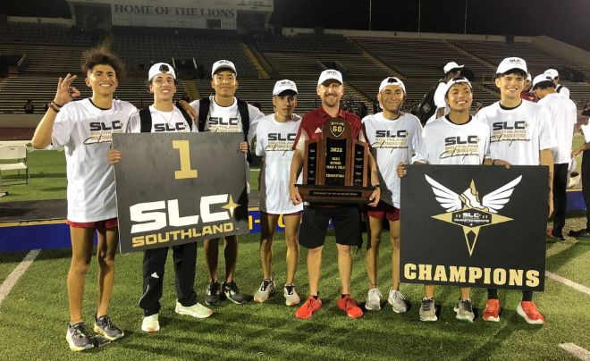 Men's track and field student-athletes with head coach holding the trophy