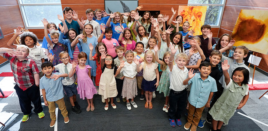 Group of children waving and smiling at Festival of Faiths