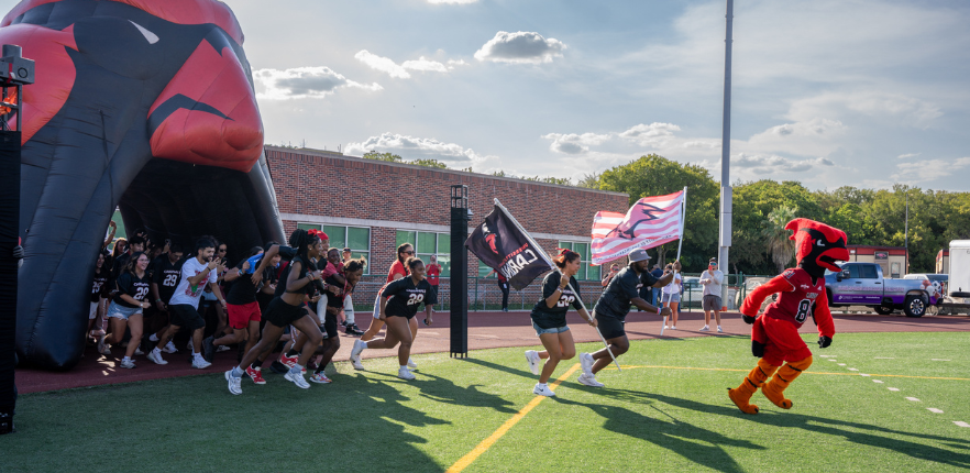 Red the Cardinal and students running across football field