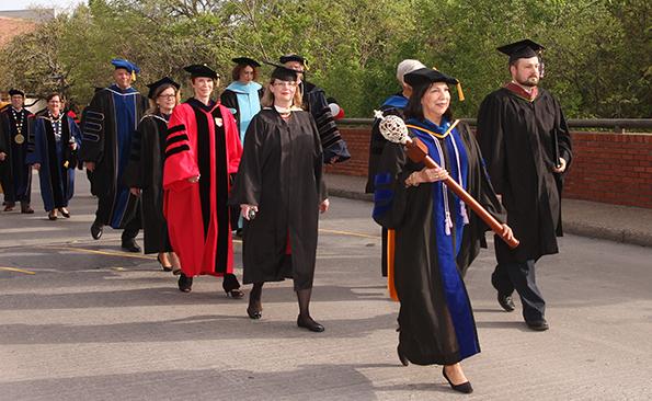 Dr. Laura Munoz leads the academic procession while holding the University Mace