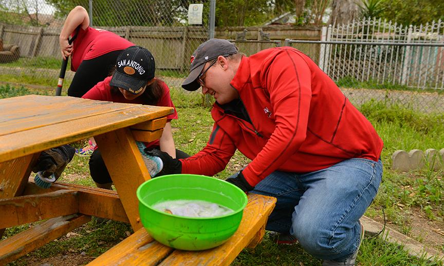Volunteers add a layer of coating to a picnic bench