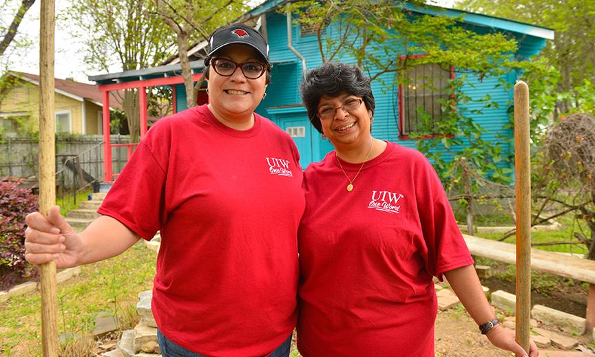 Two volunteers pose in front of a house