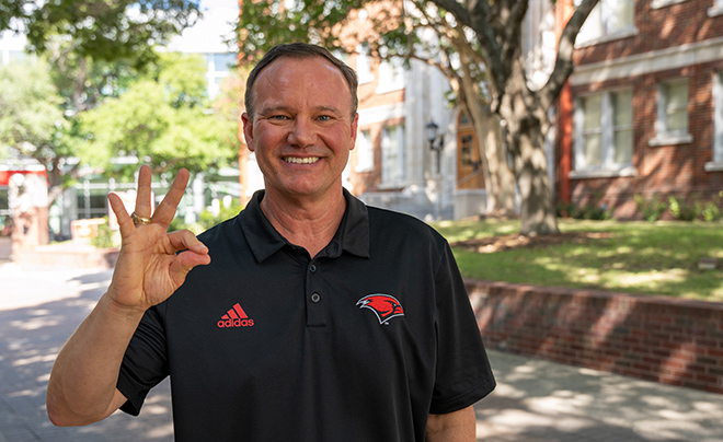 UIW President Thomas Evans in black shirt making Cardinal fingers sign