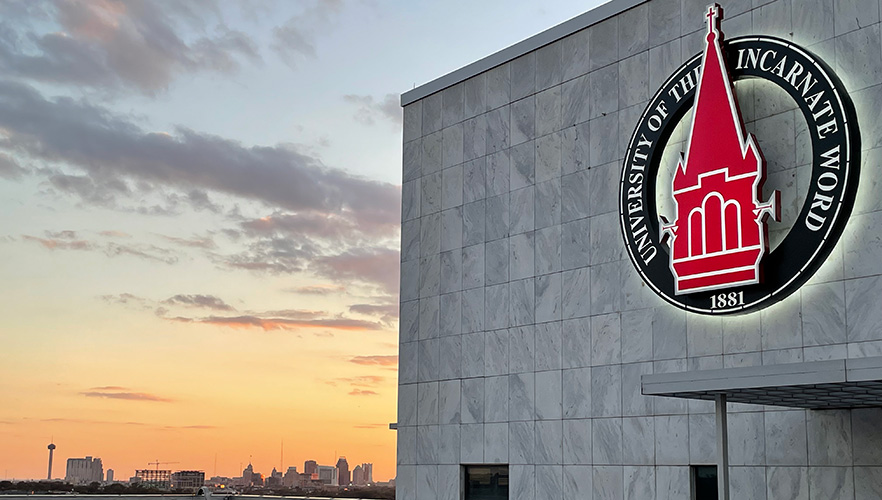 UIW logo on building with San Antonio skyline background