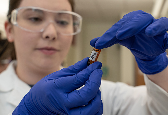 Student in goggles and a lab coat with a vial