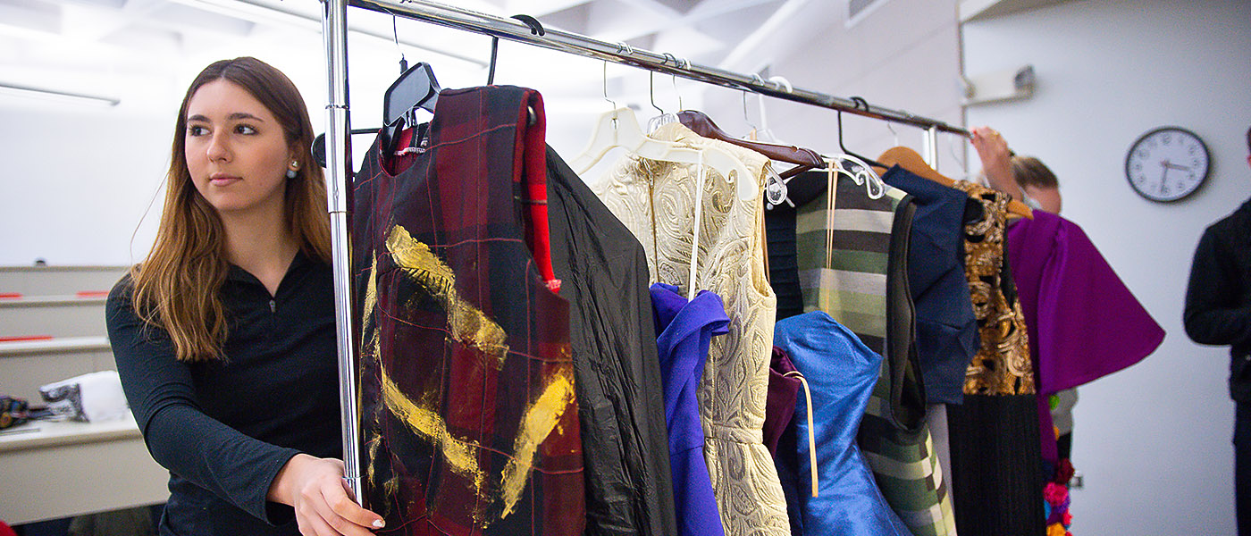 Fashion student moving a rack of designer dresses through the dressing area