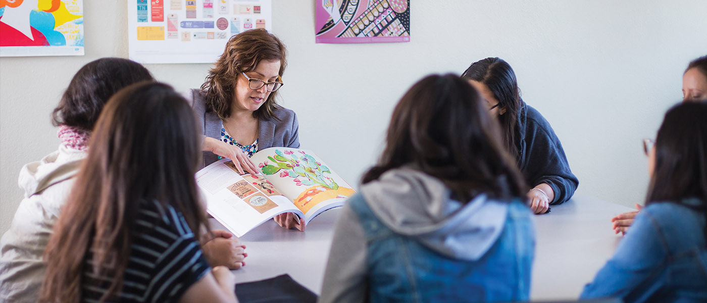 group of graphic design students listening to their professor as she shows them work in a design book