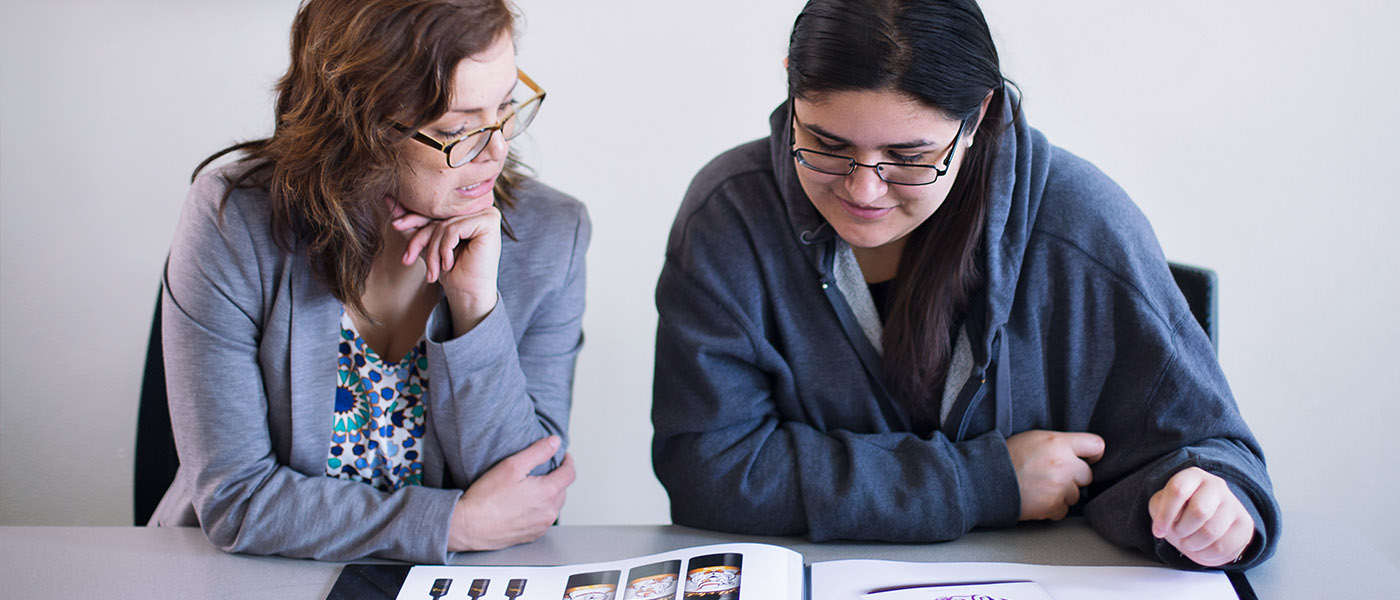 Professor going over samples of design work in a book with a student