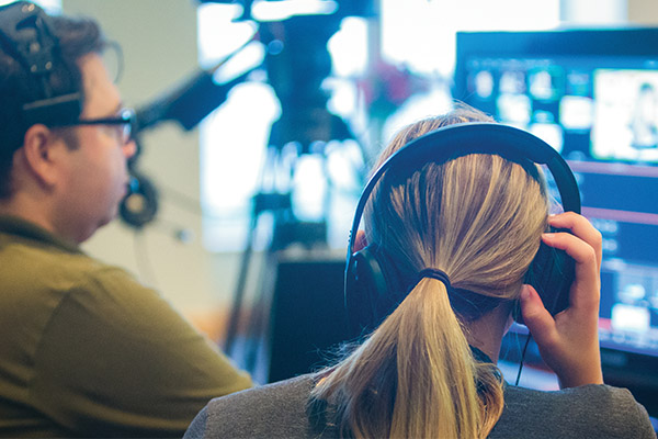 Over the shoulder view of communications students sitting in the studio working on a broadcast