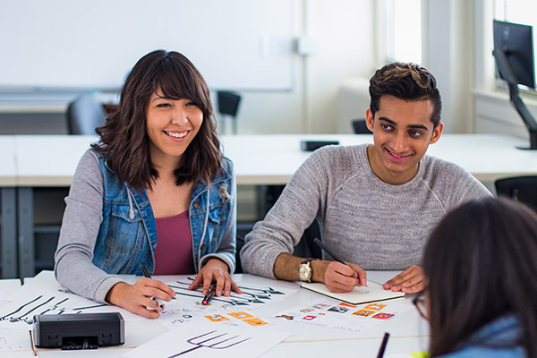 Smiling design students sitting at a table discussing their work