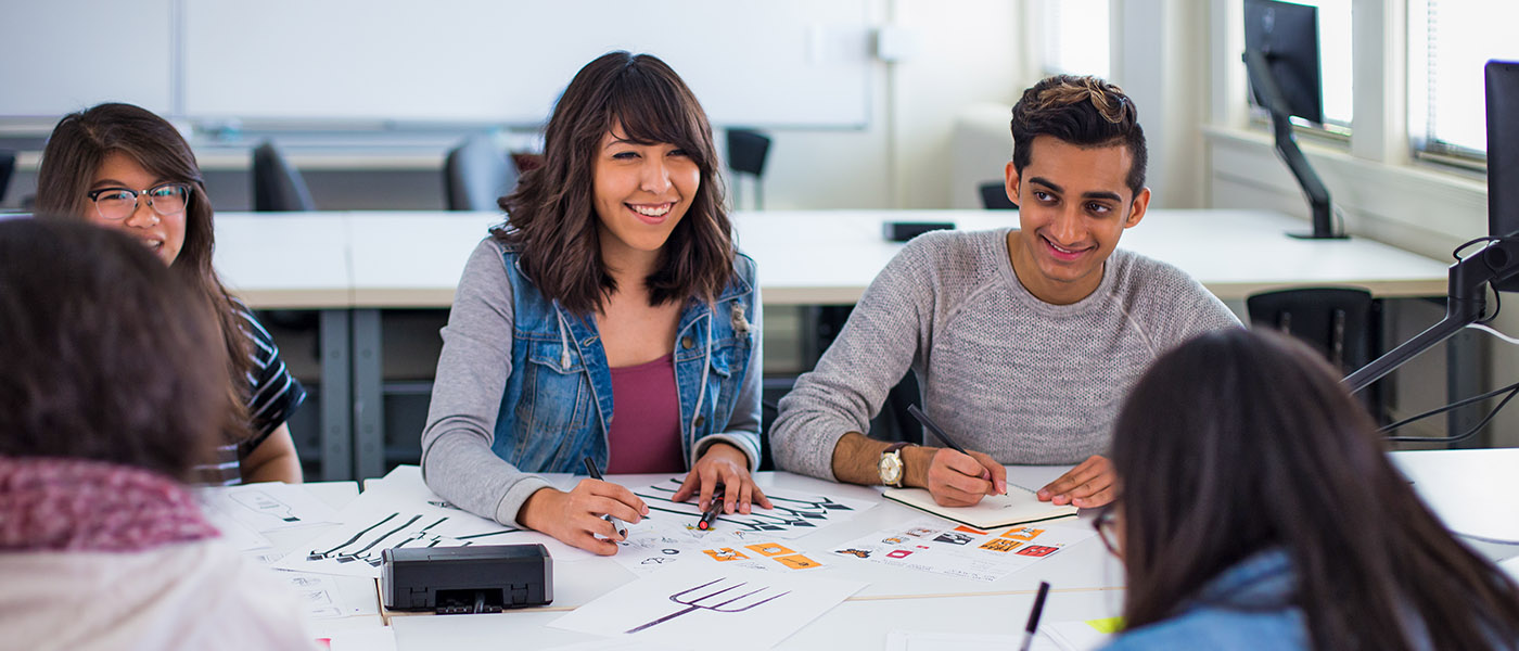 Smiling Graphic Design students in class having a conversation as they look over their projects