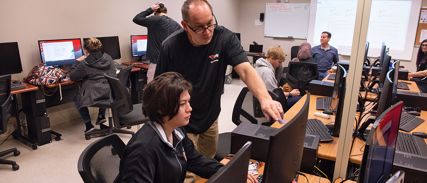 Instructor in an information security class pointing out important information on a computer screen to a student