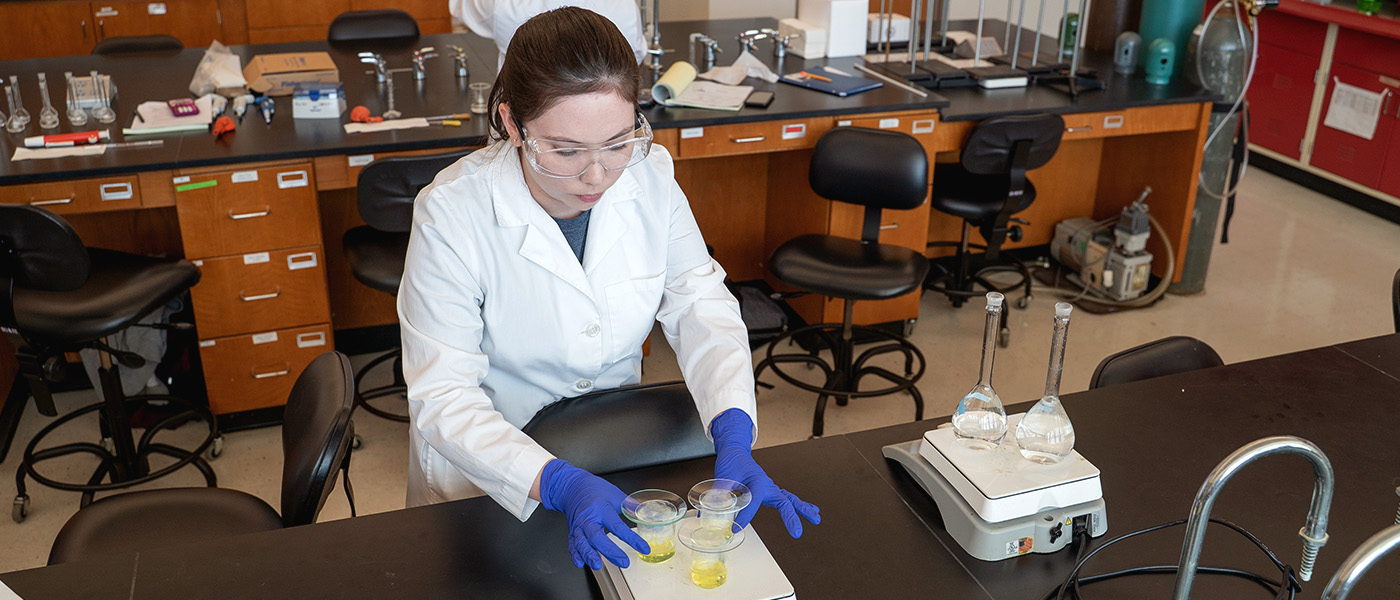 Chemistry student heating a yellow substance on a hot plate in a lab