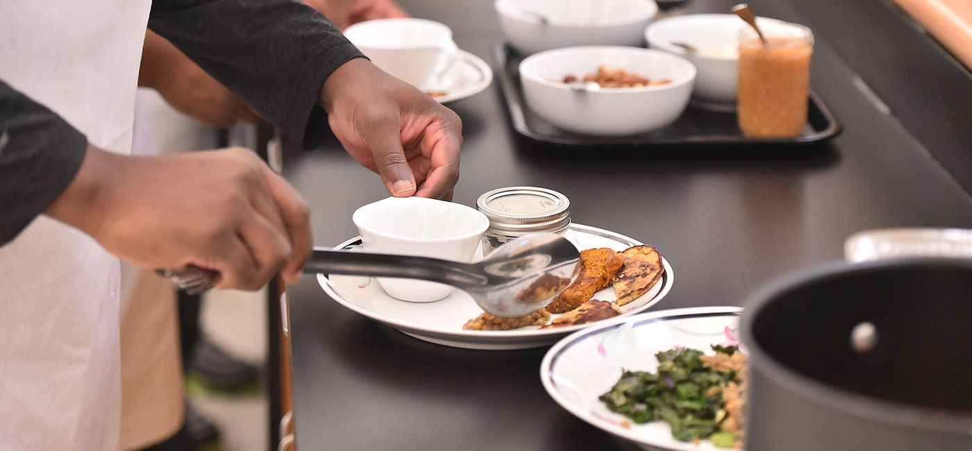 Close-up photo of a student's hands preparing food on a plate