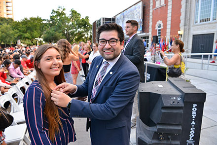 2019 alumni board president pinning lapel pin on incoming female student both looking at camera with smile in front of fine arts building