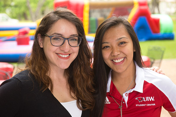 Two female students smiling with campus activities happening in the background