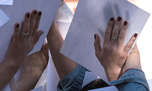 Close up of several hands holding up sheets of paper